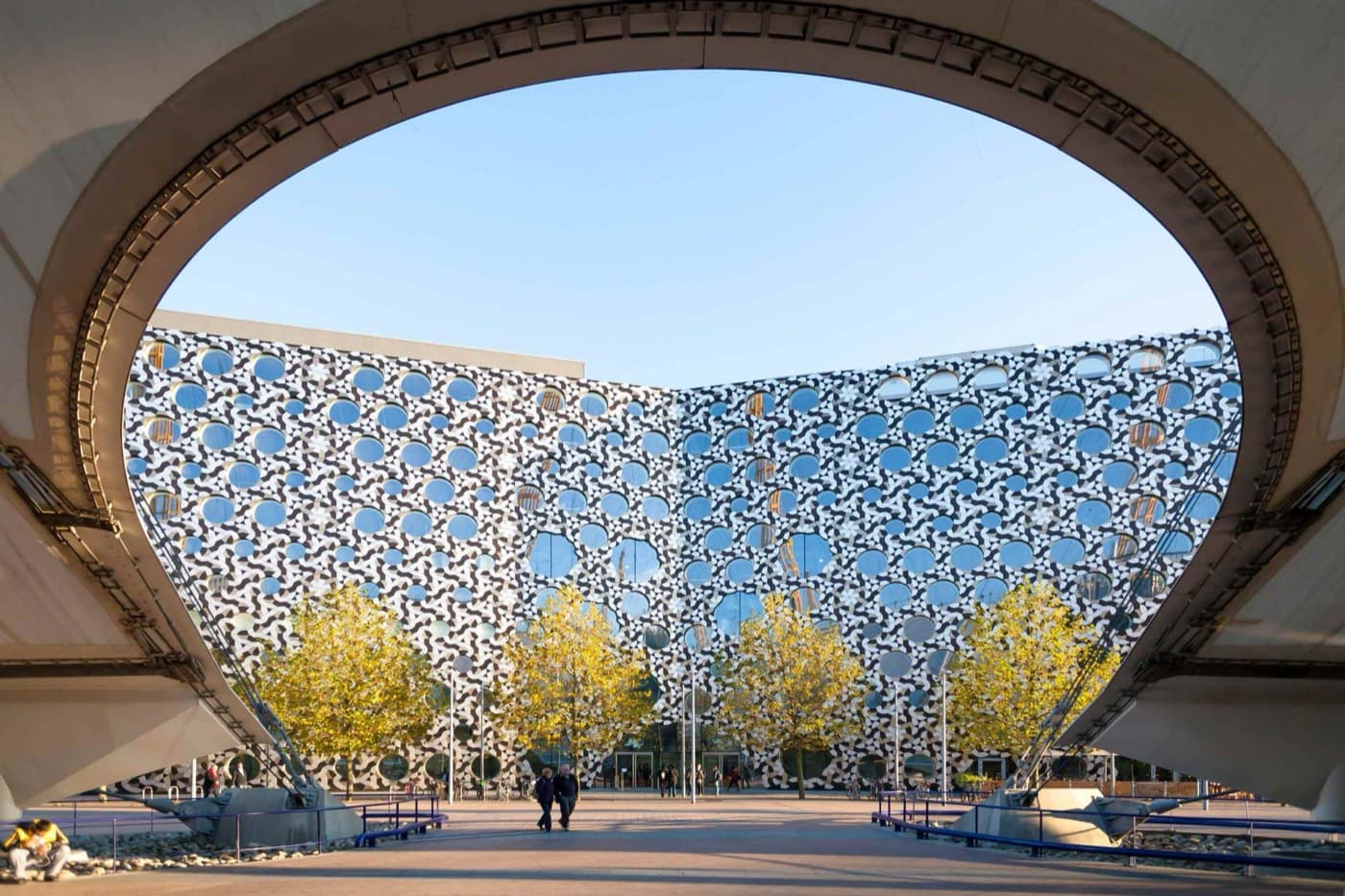Dairesel pencereli, geometrik desenli cephesiyle Ravensbourne binası, The O2’nun taşıyıcı kemerinin altından görünüm