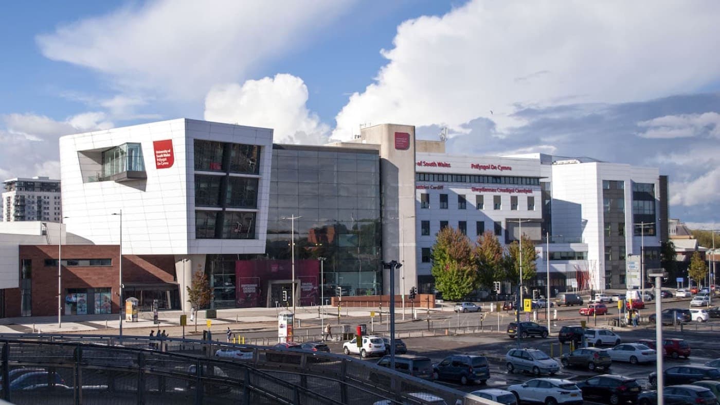 Cardiff kampüsünün modern binası ve cephesindeki University of South Wales / Prifysgol De Cymru yazısı